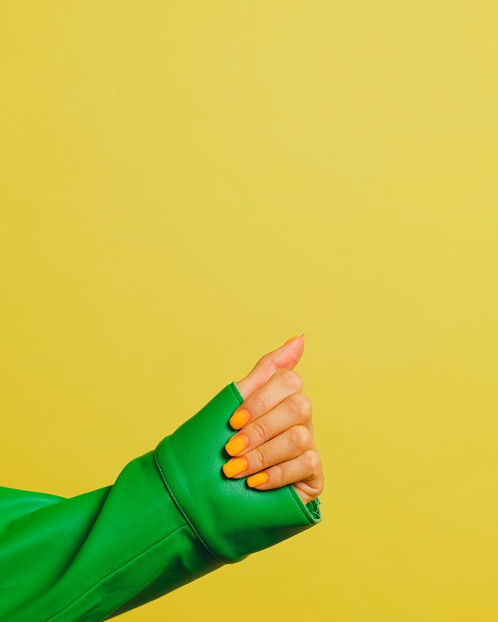 Bright orange nails against a yellow wall