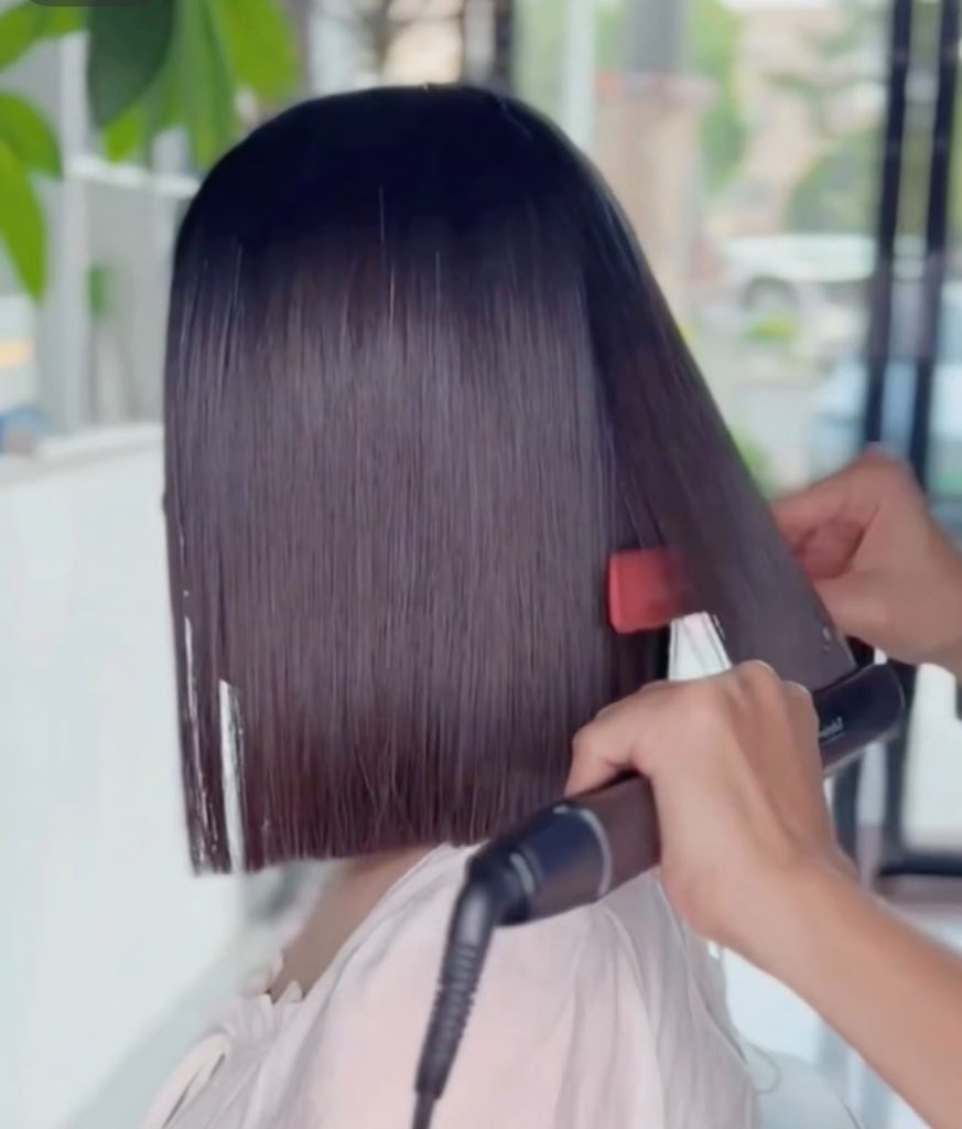 A stylist straightening a sleek bob with a flat iron during rebonding